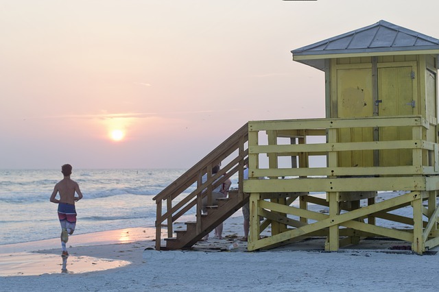 Man running on beach next to lifeguard tower.