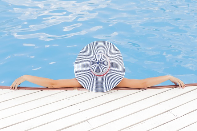 A woman wearing a hat in a pool, representing one of the ways to avoid sunburn.