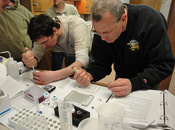 Fishermen Mikhail Shablin (left) and Robert Clement (right) perform scientific lab tests aboard the F/W Melissa K, making the initial determination about whether the clams they just caught are safe to eat. The men were trained by FDA staff.